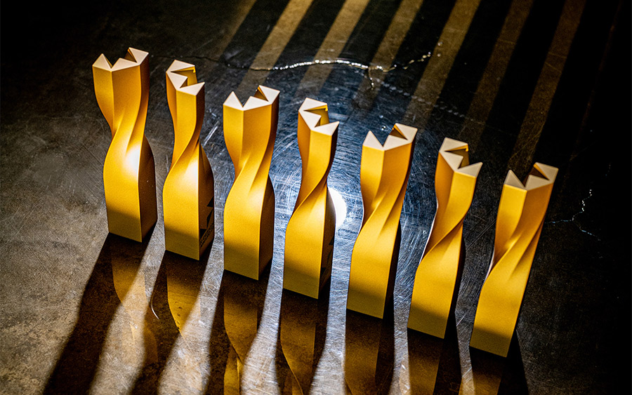 Siete trofeos K-Design Award dorados vistos desde arriba, con la torsión en hélice y el remate de muescas en V que forma el logotipo